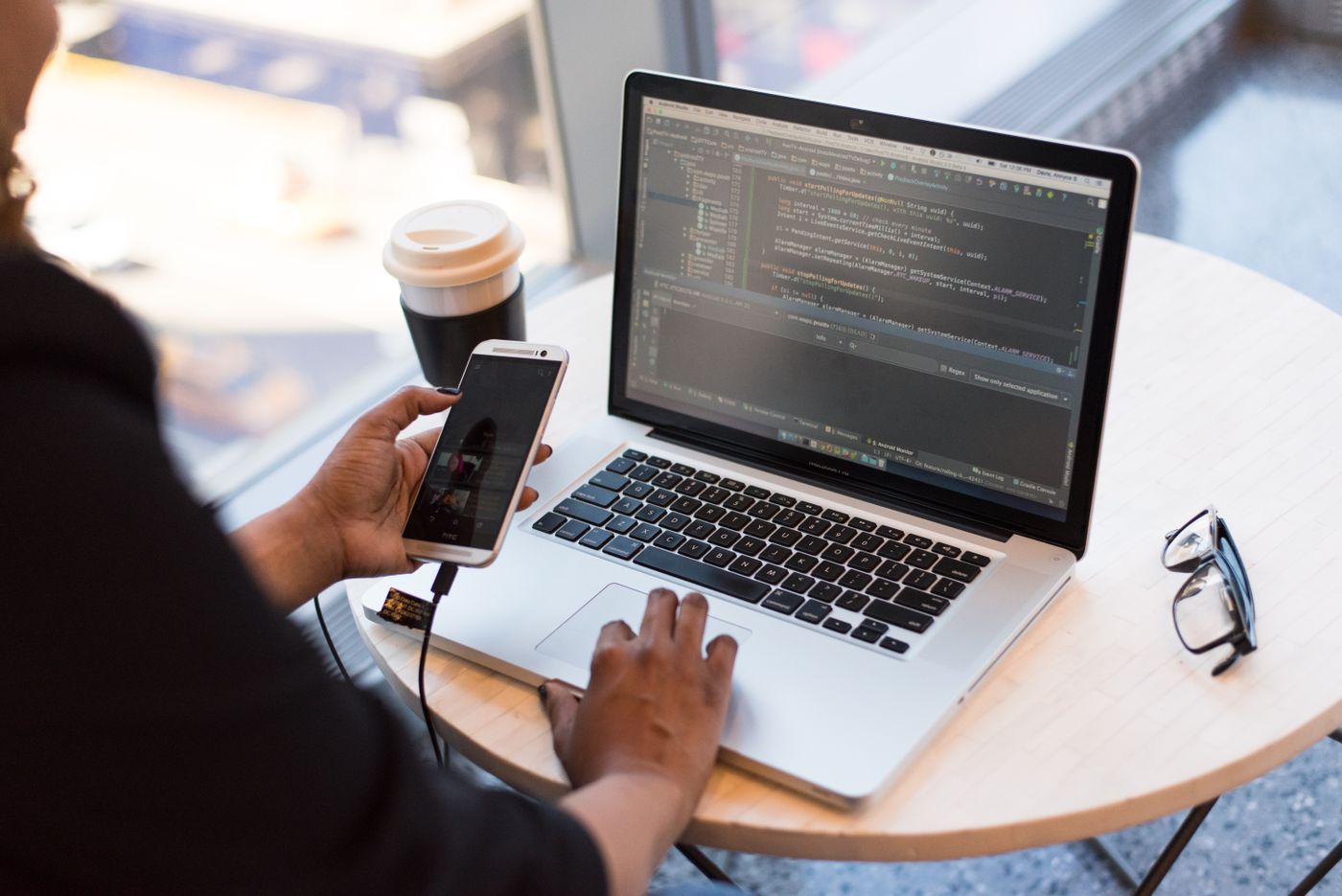 Profissional trabalhando no notebook com o celular em mãos